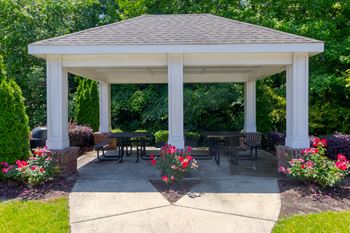 A white gazebo with a brown roof is surrounded by flowers and greenery.